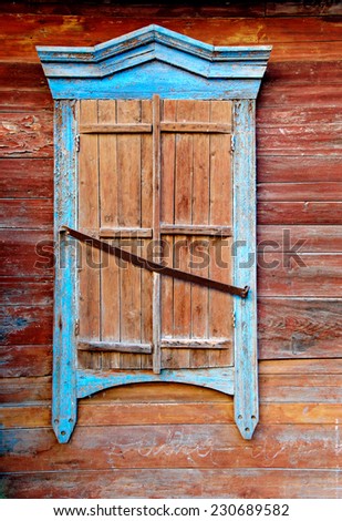 Vintage window of wooden hut in traditional Russian style in Astrakhan, Russia. Closeup detail of the exterior of wooden house. Window with closed shutters painted in brown and bright  blue color
