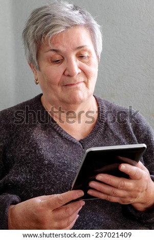 Vertical portrait of a Caucasian senior good looking woman smiling and holding a PC tablet. Grandma Using Tablet PC in Living Room