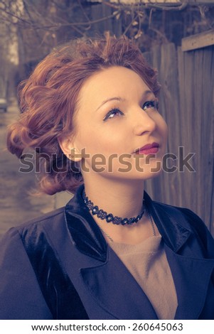 Woman with messy retro coiffure posing outdoors wearing black coat head and shoulders image. Toned , film color imitation