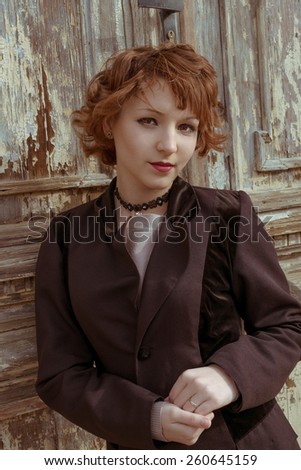 Retro portrait of red haired women in vintage coat agains obsolete wooden background.