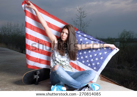 Girl is posing with stars and stripes US flag. Casual trendy girl posing with american flag and skateboard sitting  crossed legs outdoors.  Evening shot. Instagram filter. Independence day celebration
