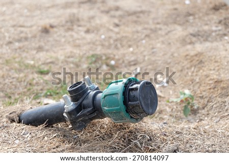 Field hosepipe sprinkler end, bare soil, copyspace. Plastic pipe is sticking out from the ground with blind stopper cap. A lot of copy space.