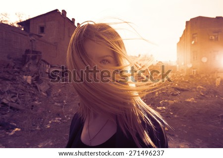Women walking in slums. Loneliness. Portrait full of sunset sunshine. Backlit image of blonde girl with wind in her hair.Focus on eyes. Instagram color.Her face is half hidden by hair flying with wind