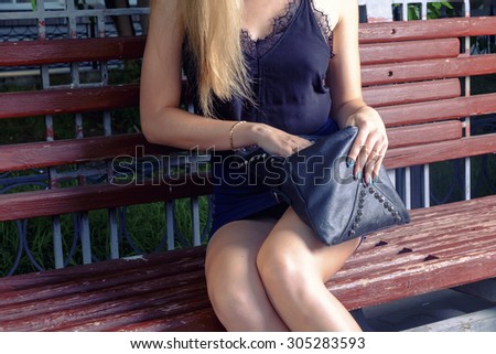 Fashionable stylish young woman open black handbag on park bench