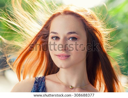 Young fresh redhead women looking at camera. Her hair fly with the wind. Backlit by sun.