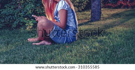 Young woman using tablet outdoor is sitting on grass, no face, side view. Copyspace. A lot of space for text