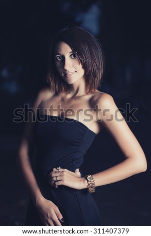 Attractive elegant female in gorgeous evening dress is posing in romantic fashion manner happy expression on her face.Sexy rich party girl.Luxury lifestyle.She is half lit from side with harsh shadows