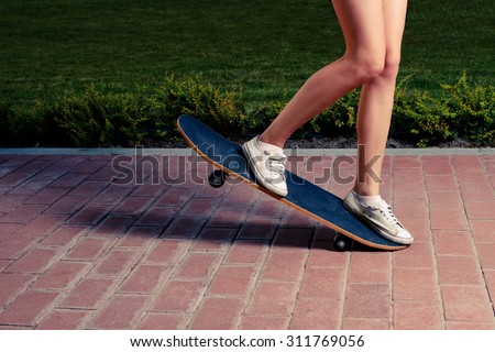 Young women is doing a trick on a skateboard toned image warm color. A lot of space for text. Legs of slim sporty girl riding scateboard on paved surface