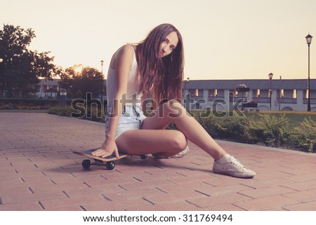 Cute girl is sitting on her skateboard backlit. Street life. Urban style of life. Youth culture. Urban sport. Instagram style image. Warm color toned pocture. A lot of space for text