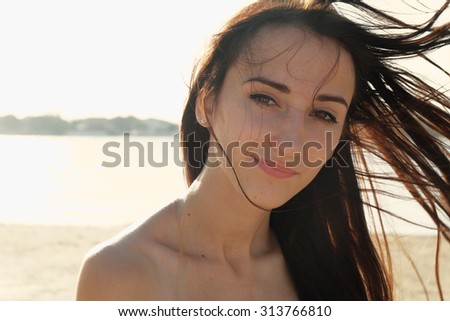Portrait of young girl on the beach. Her hair fly with the wind. She is looking at camera with pensive face. Thoughtful woman. Toned in warm colors. Outdoors shot, lifestyle.Freedom attire