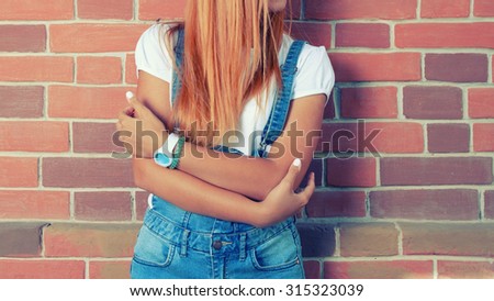 Young beautiful blonde woman in boiler suit (jeans overalls) on red brick wall background. Hipster girl no face shot,  a lot of space for text
