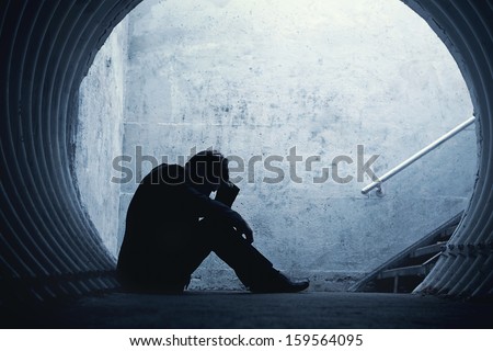 Desperate Businessman in silhouette lying on the ground and holding his head in a dark tunnel. With room for your text