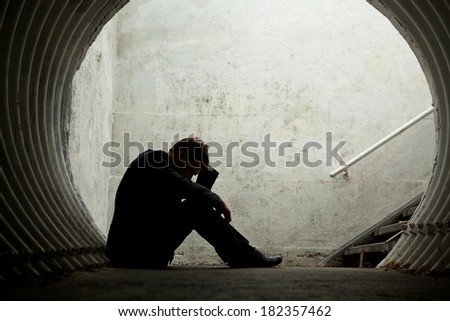 Desperate Businessman in silhouette lying on the ground and holding his head in a dark tunnel. With room for your text