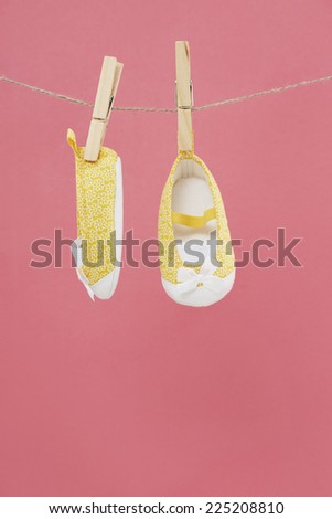 Baby shoes hanging on washing line against pink