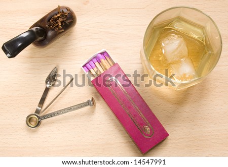 Overhead shot of a pipe with tobacco, a glass of whiskey, a box of long matches and a cleaning tool on a wooden table.