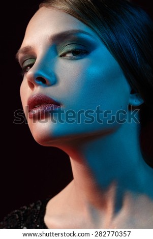 Close portrait of a girl in an elegant jacket, smokey makeup, blue and red lights, styled hair.