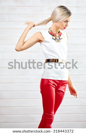 Beautiful fashionable slim girl standing in red leather pants, a white tank top and gold jewelry.