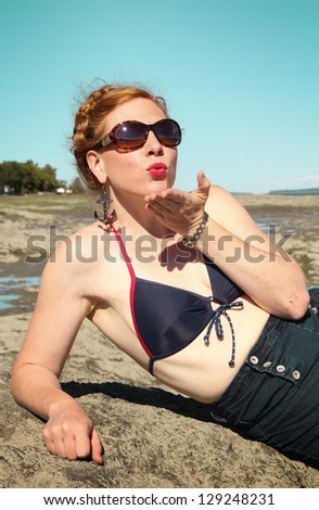 Red hair woman sending kiss and posing on a rock in a swimming suit vintage style