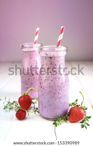 Berry smoothie with strawberry, red straw  and herbs in a little milk bottle