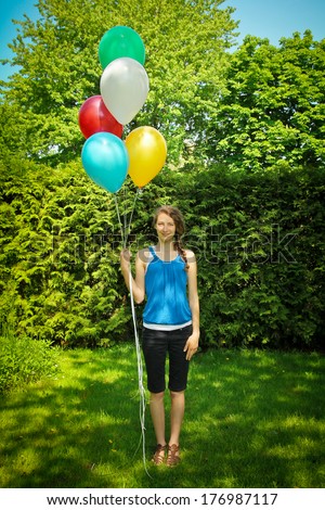 Teen standing on grass holding a bunch of balloons