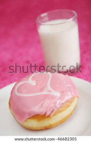 Pink donut with heart and a glass of milk in background
