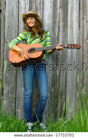 Young girl with a cowboy hat holding guitar against a barn