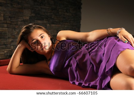 Young girl wearing a purple satin dress laying on a red floor