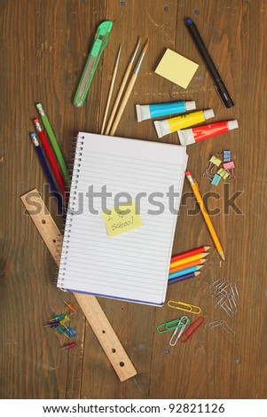School material, pencil, rule, brushes, paper clips on a wooden table with a note book with a postite with \