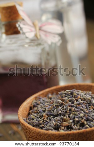 Dried lavender in a wooden bowl with lavender oil in a background