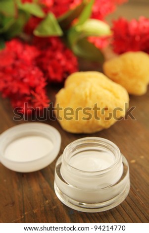 Cream with natural sea sponge and red flowers on a wooden table
