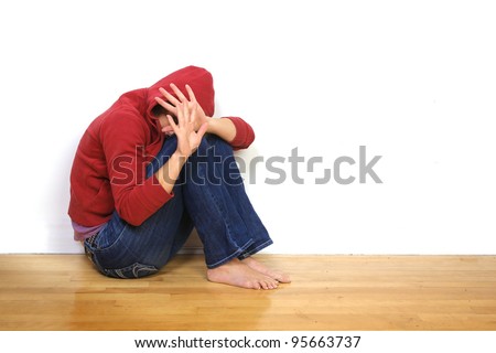 Scared woman with hood on head sit against a wall and protecting herself with open hands