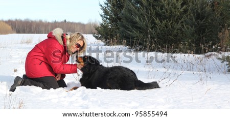 Woman with red jacket laying in snow with her dog