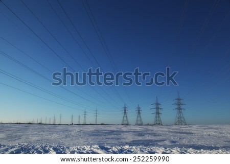 Group of high-voltage electricity power pylons over blue sky and snow covered countryside, Canada