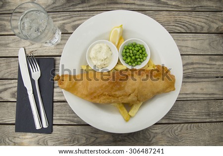 Fish and chips served with tartar sauce, green peas and lemon on a rustic background