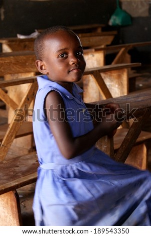 MATUGGA, UGANDA, AFRICA - CA AUGUST 2013: Unidentified young girl in a blue school uniform sitting on an old fashioned wooden school bench in a classroom. North of Capital Kampala, Uganda, East Africa