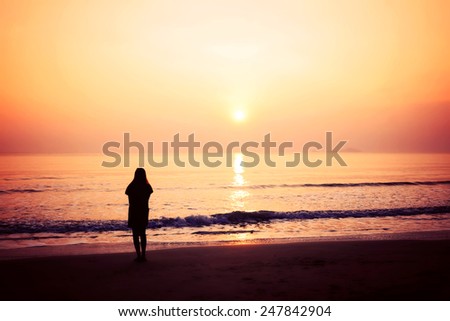 silhouette of woman alone and wave on the beach with sunset in the sea, blurred