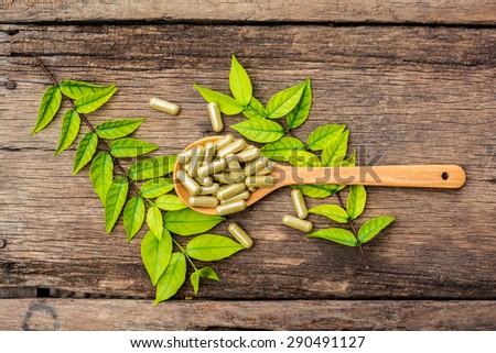Herbal medicine capsules in spoon with leaf of plant on old wooden background