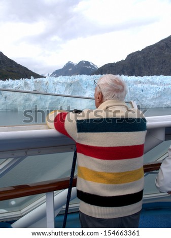An older man views the Ried Glacier in Glacier Bay, Alaska from the deck of a cruise ship.
