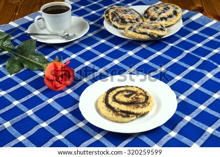 Homemade cake with poppy seeds in the shape of a snail with a cup of coffee, red rose on a blue placemat, sweets, dessert