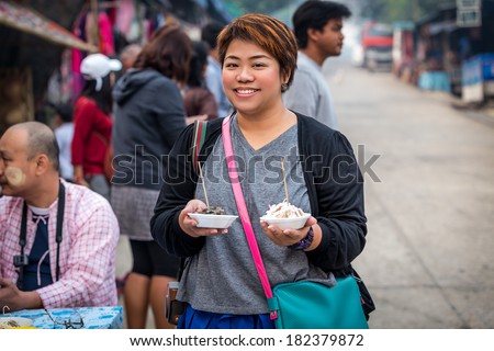 Kanchanaburi,Thailand-March 9 2014:Asian woman smiling with local  street food in her hands in front of the morning market of Kanchanaburi ,Thailand