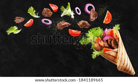 Doner kebab or shawarma with ingredients floating in the air : beef meat, lettuce, onion, tomatos, spice. Black background. Copy space.