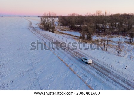 Aerial photo of a white SUV driving down a snowy road in rural North Dakota. Snow is blowing across the road and barren, brown vegetation surrounds the road. Beautiful sunset. Winter. Foto stock © 