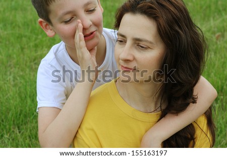 A preteen boy is clasping his mother in his arms and whispering anything hers outdoors.
