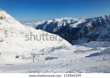 Skiers are sliding down snow-covered hill at the Cirque du Lys. There is range of mountains in the background. Winter Pyrenees is photographed at the Cauterets ski resort.