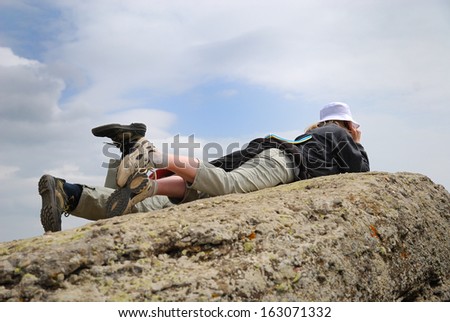 Woman and teenage boy are lying on the top of mountain against the sky. Both tourists are resting.