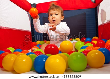 Baby boy sitting in playpen with colorful balls and throwing a orange ball