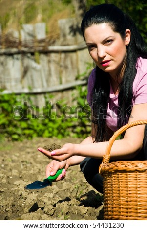 Young farmer woman  in a garden holding soil and garden tool in her hands
