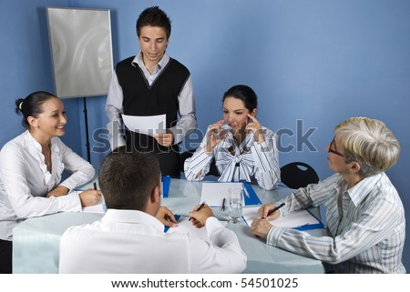 Business meeting with group of people,a businessman making a speech and reading from a paperwork and a businesswoman drinking water and thinking while the others having a conversation