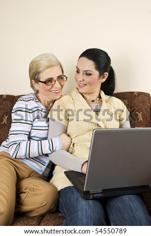 Two women sitting on sofa,using laptop and having a funny discussion and laughing together