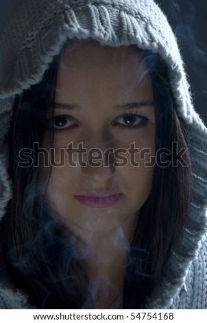 Young woman with wool hood in darkness with smoke around her